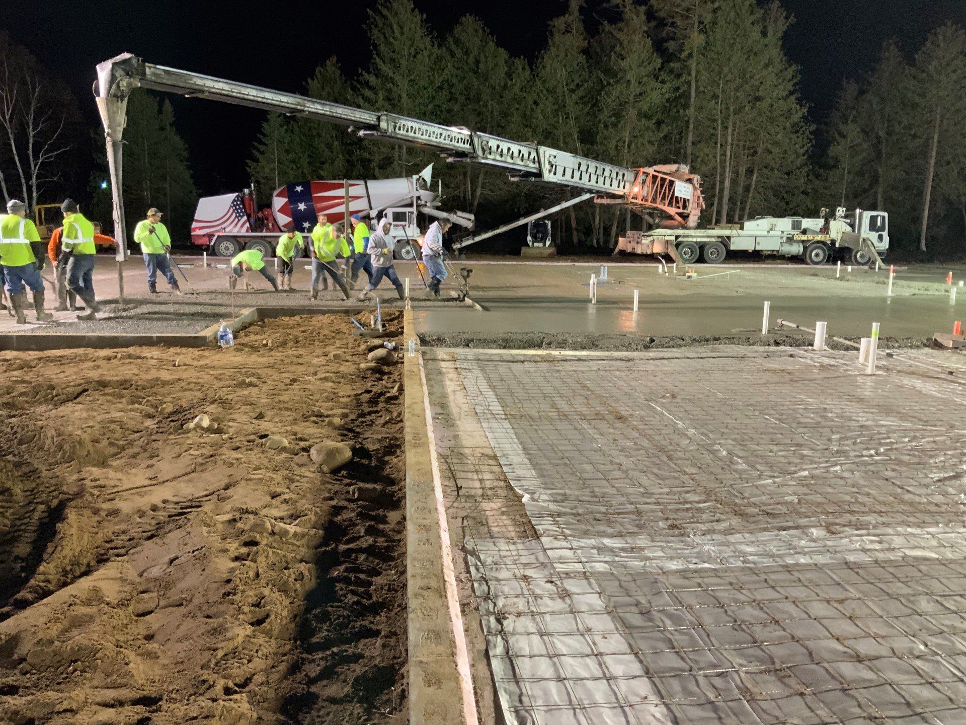 A group of construction workers are working on a concrete floor at night.