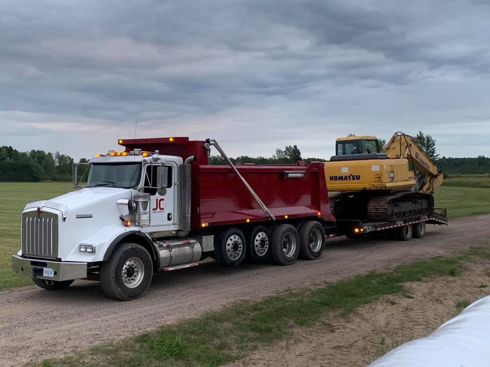 A dump truck is carrying a large excavator on a trailer.