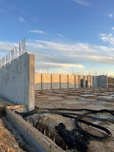 A large concrete wall is being built on top of a dirt field.