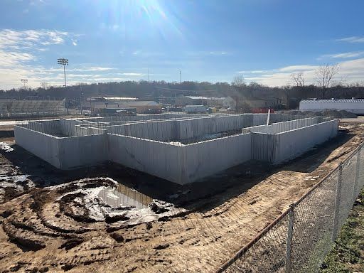 A large concrete wall is being built in a dirt field next to a fence.