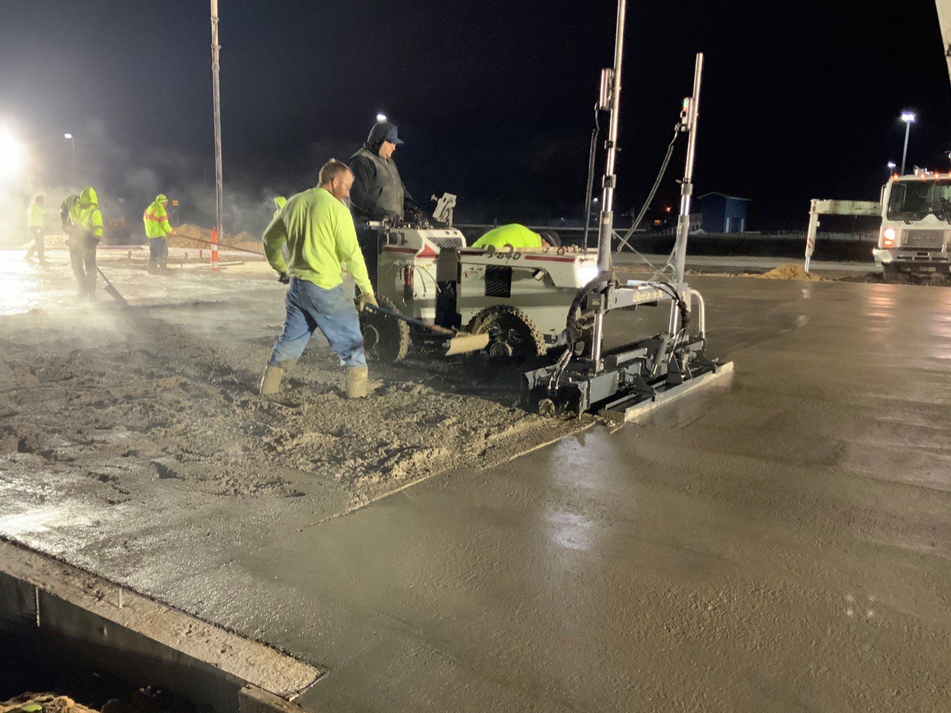 A group of construction workers are working on a concrete floor at night.