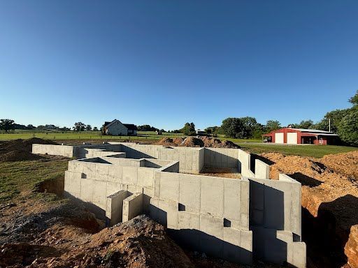 A concrete foundation is being built in a field with a red barn in the background.