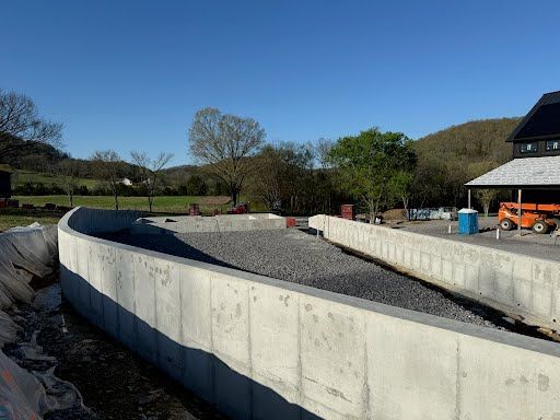 A large concrete wall is surrounded by gravel and a building in the background.