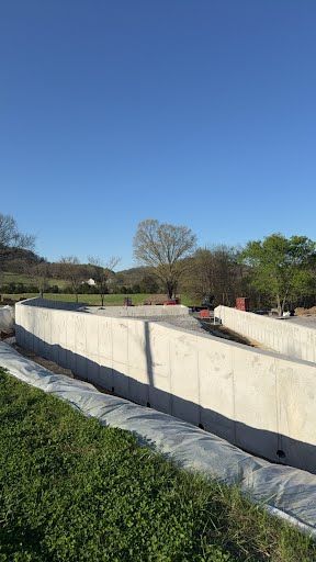 A large concrete wall is surrounded by grass and trees in a field.