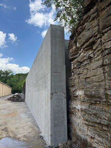 A large concrete wall is sitting next to a stone wall.