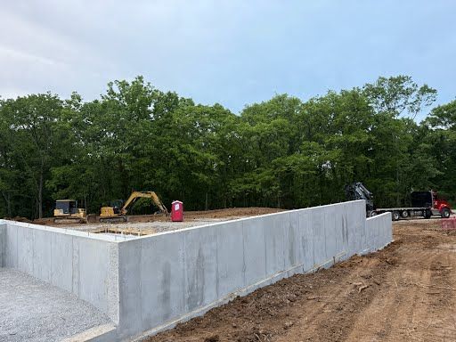 A concrete wall is being built in a dirt field with trees in the background.