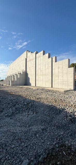 A large concrete retaining wall under a blue sky; the ground is covered in gravel.