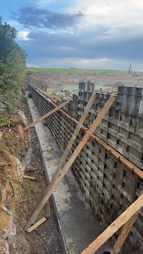 Construction site: retaining wall being built with concrete blocks, wooden supports, cloudy sky.