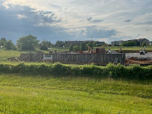 A large building is being built in the middle of a grassy field.