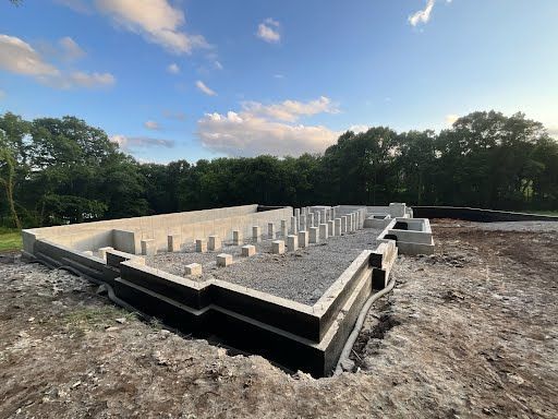 A foundation for a house is being built in a dirt field with trees in the background.