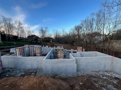 Concrete foundation walls for a new house under construction at an outdoor site with trees under a blue sky.