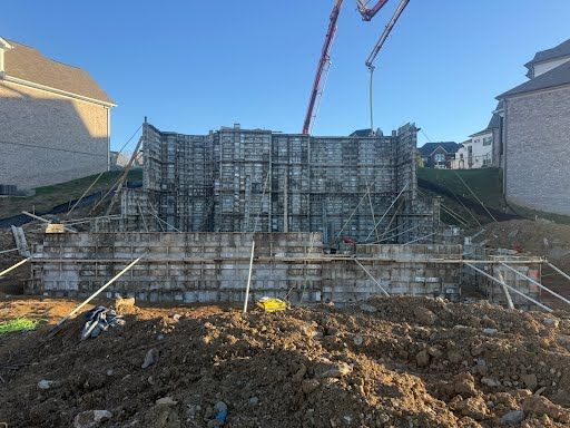 A concrete foundation under construction with metal forms, support braces, and a concrete pump boom against a clear sky.