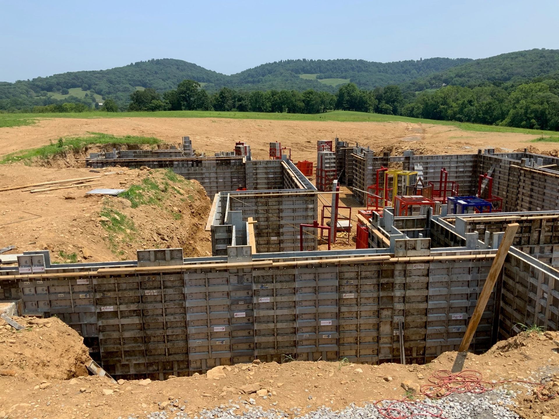 A foundation for a house is being built in a field with mountains in the background.