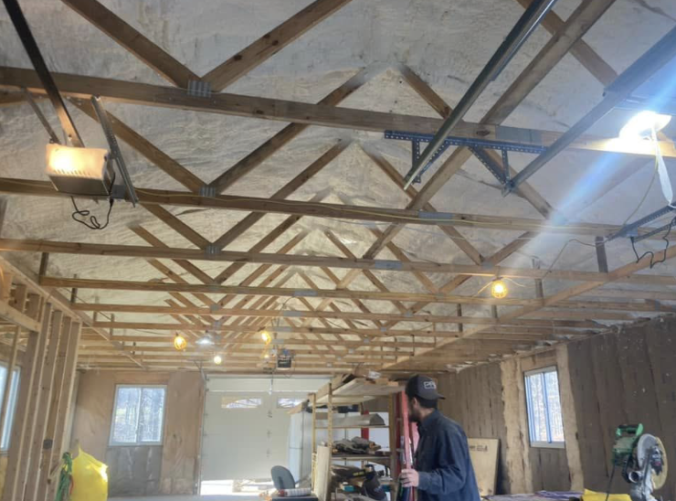 A man is spraying foam on the ceiling of a garage.