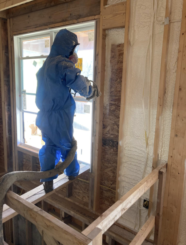 A man in a blue suit is spraying insulation on a wall.