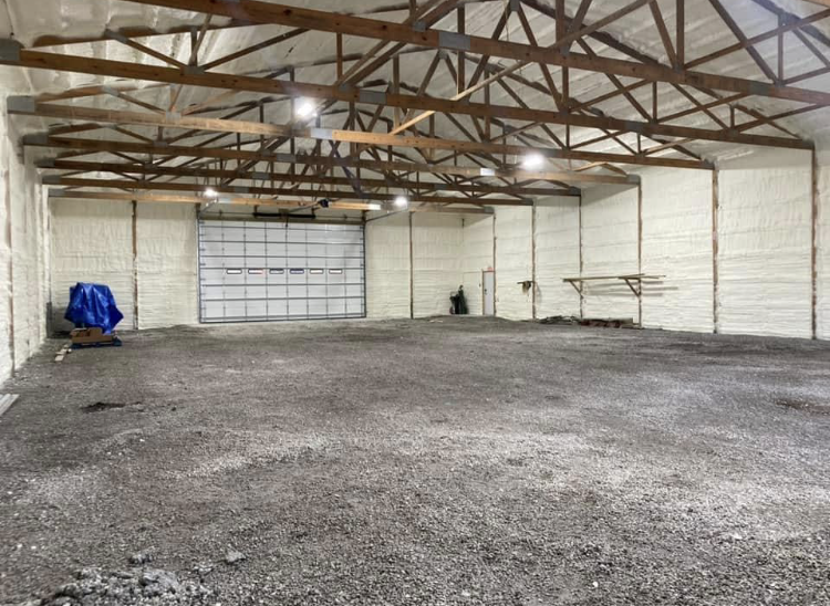 A large empty warehouse with a garage door and a gravel floor.