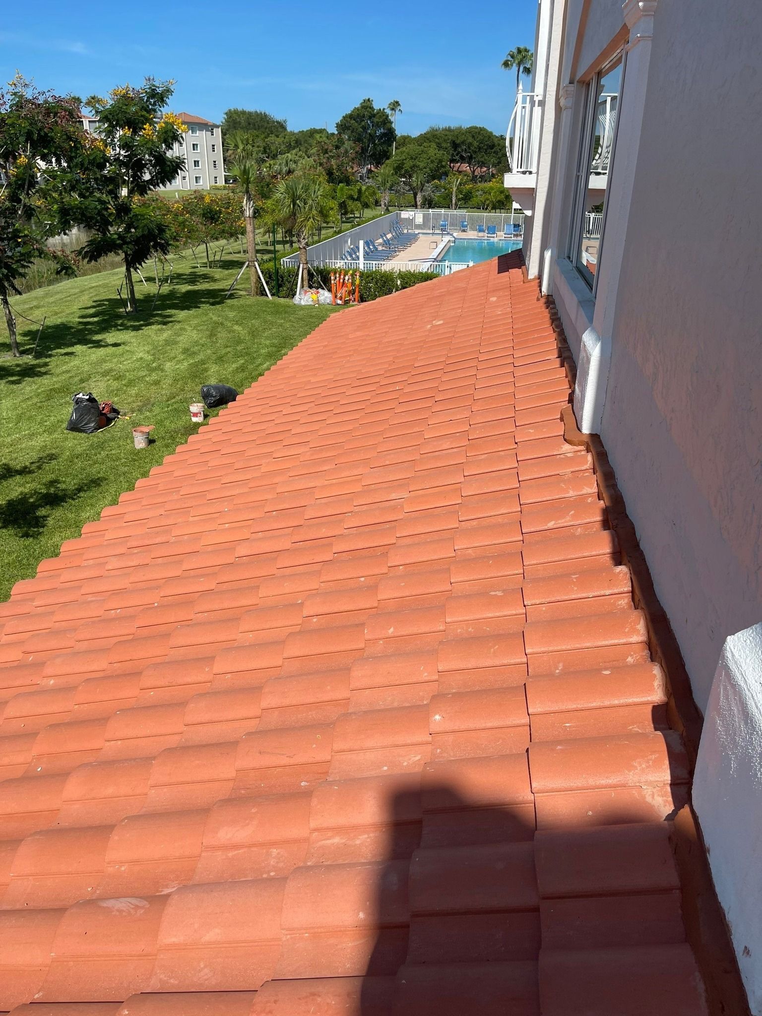 Red tile roof next to a white building. Green lawn and pool in the background, sunny day.