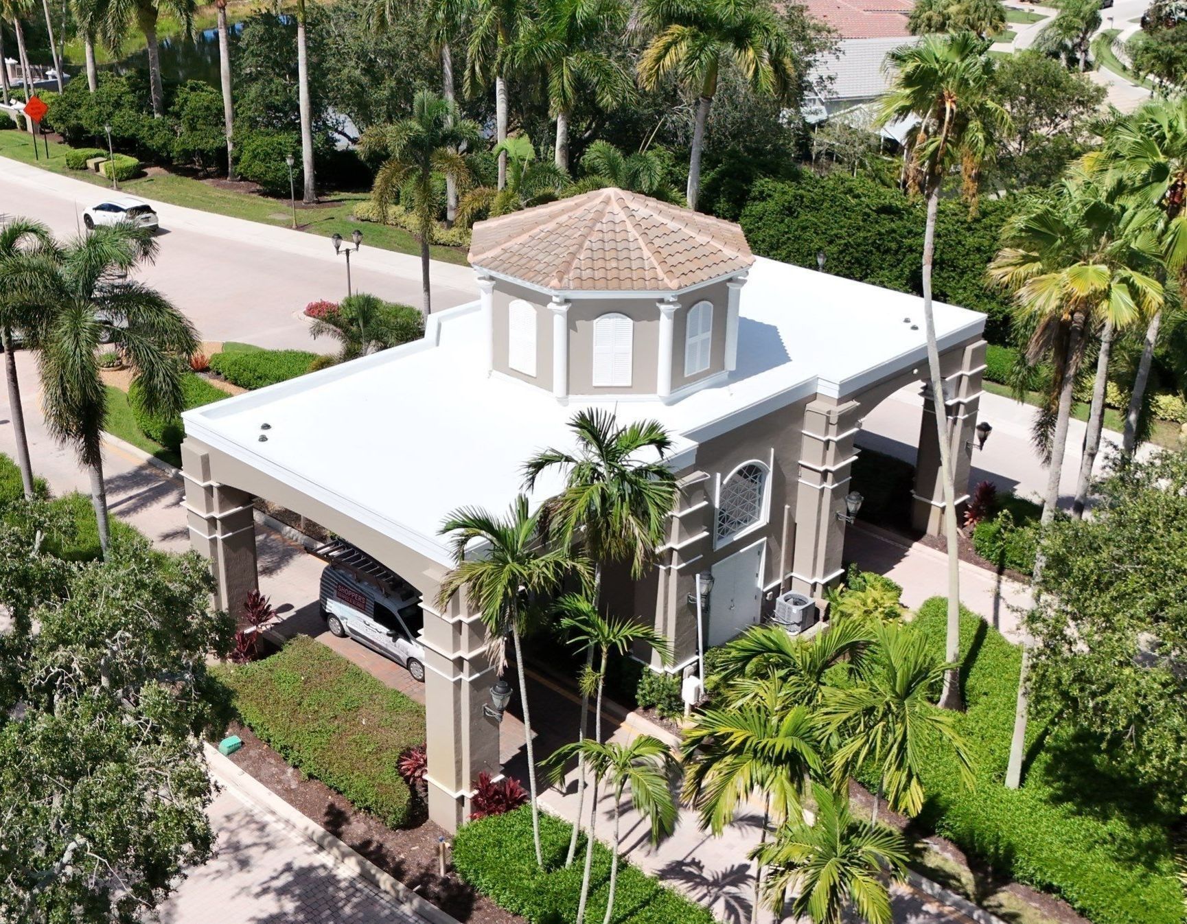 Gatehouse entrance to a gated community with palm trees and a white roof.