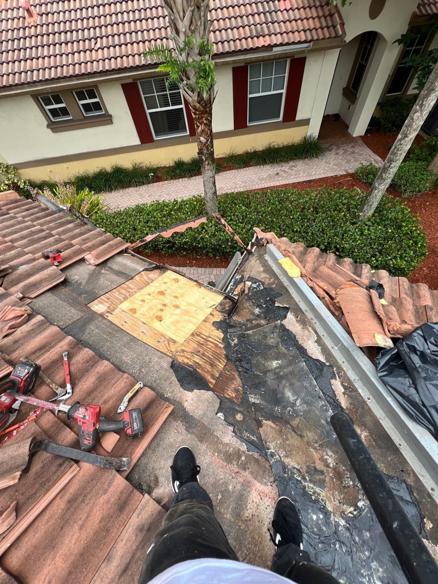 Person standing on a tiled roof, repairing a damaged area with tools.