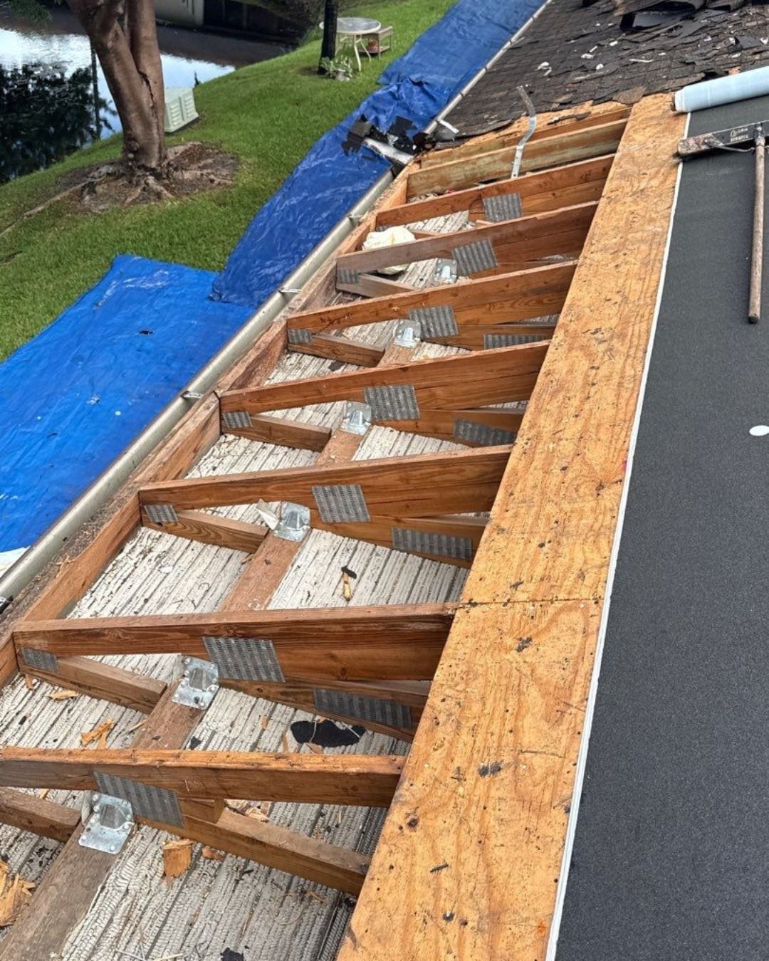 Roof under construction, wooden rafters, and support beams visible, blue tarp, black roofing.