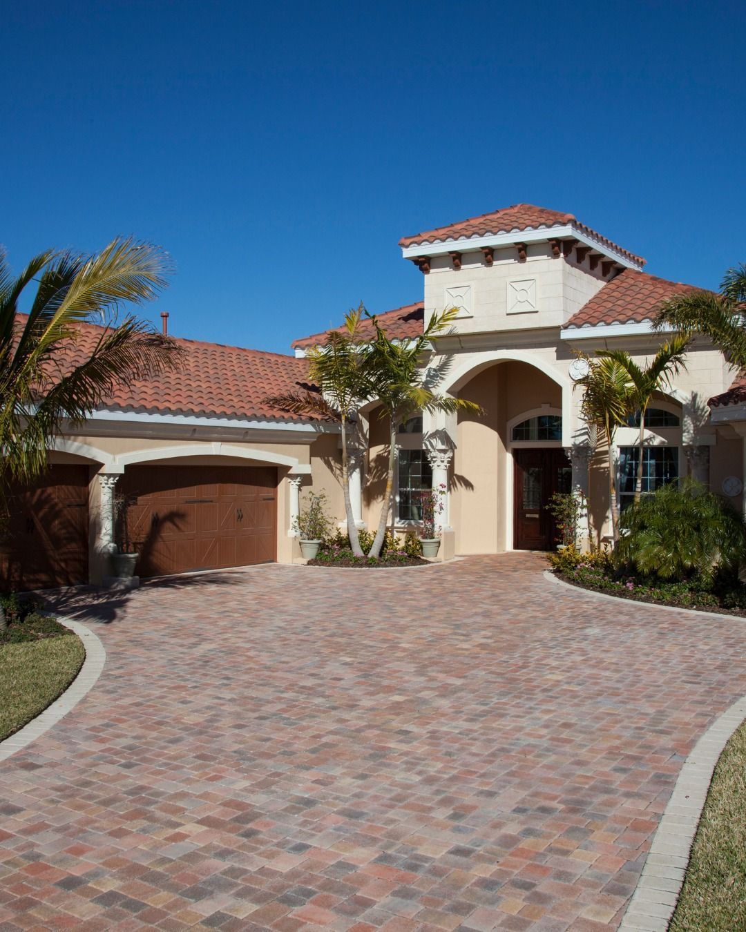 Mediterranean-style home with a red tile roof and brick driveway under a clear blue sky.