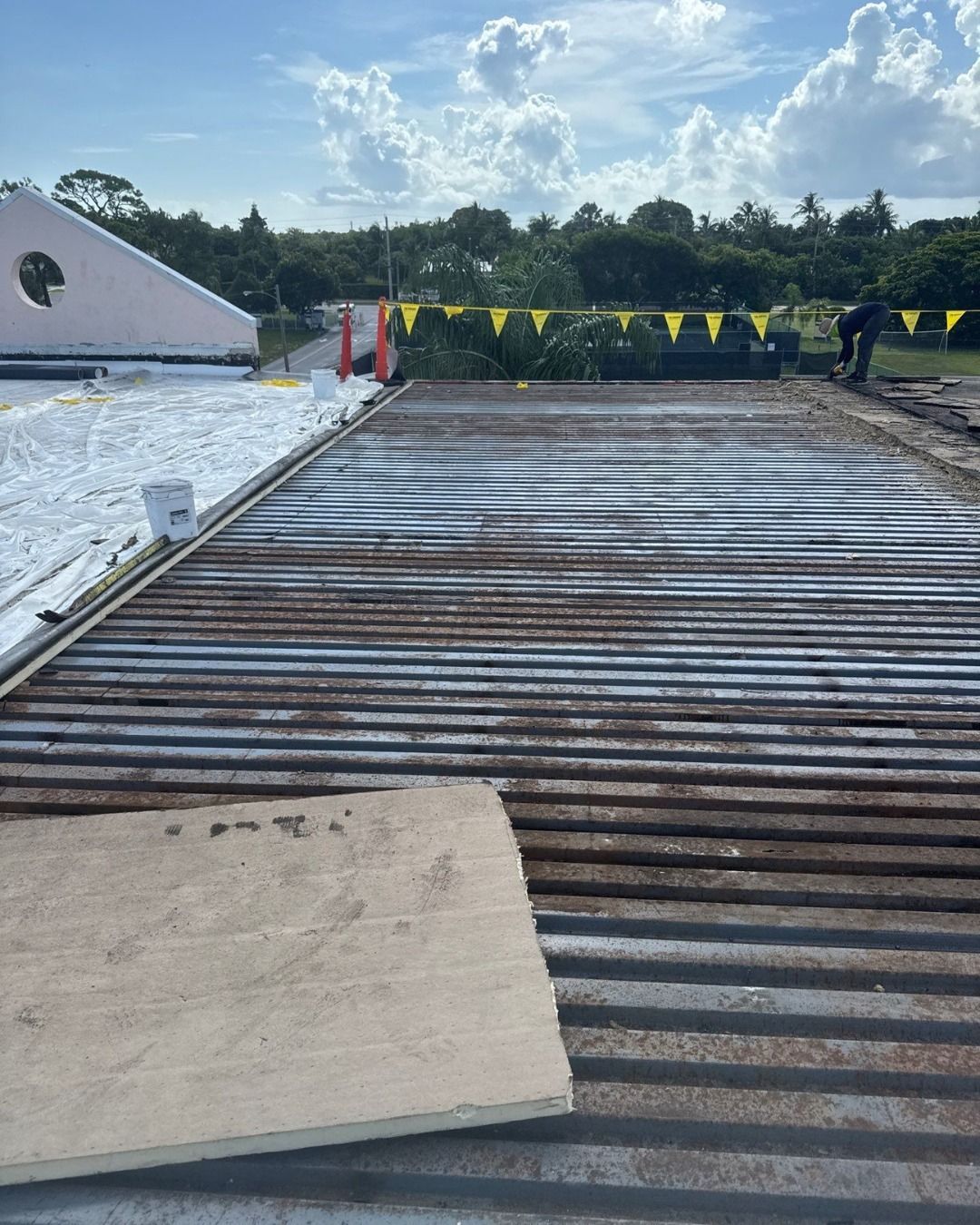 Corrugated metal roof being worked on outside under a blue sky, with safety cones and flags.