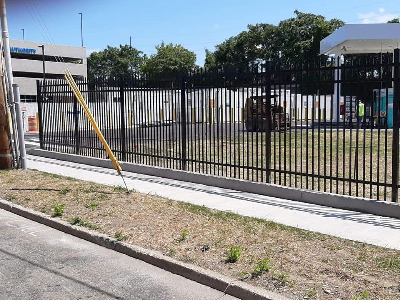 Black metal fence along a sidewalk with a gas station visible in the background.