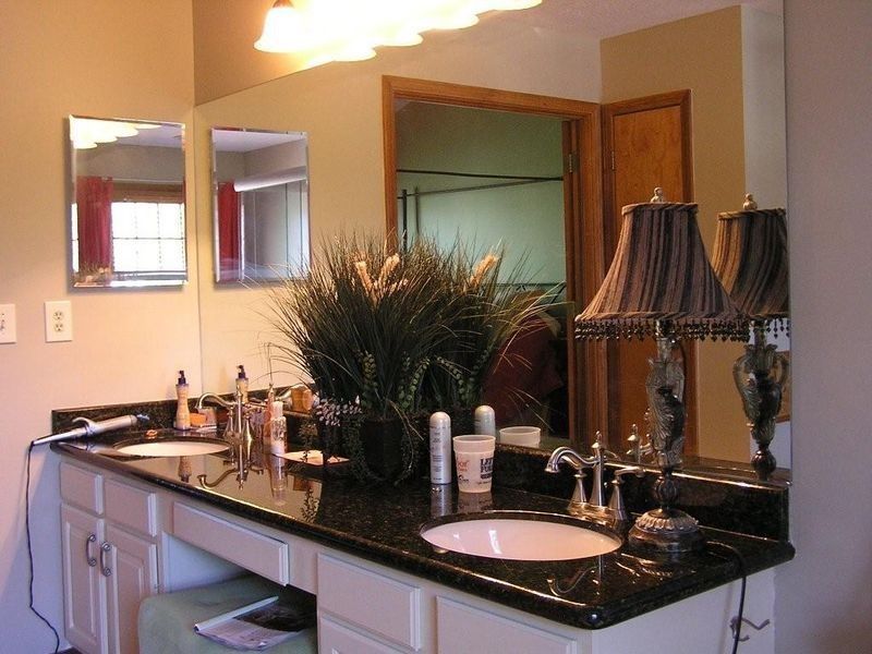 Bathroom vanity with black granite countertop, double sinks, mirrors, and lamps in a warm-toned room
