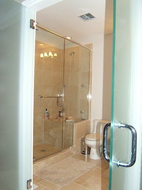 Bathroom with glass-enclosed shower, beige tile, and toilet seen through an open doorway