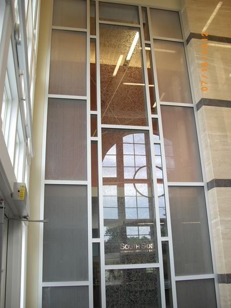 Tall glass window wall with white framing and reflections inside a bright building lobby