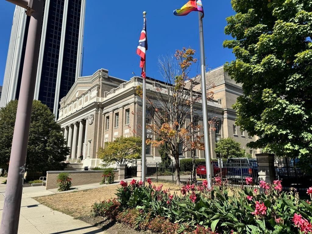 City hall building with flagpoles, flowers, and trees under a bright blue sky