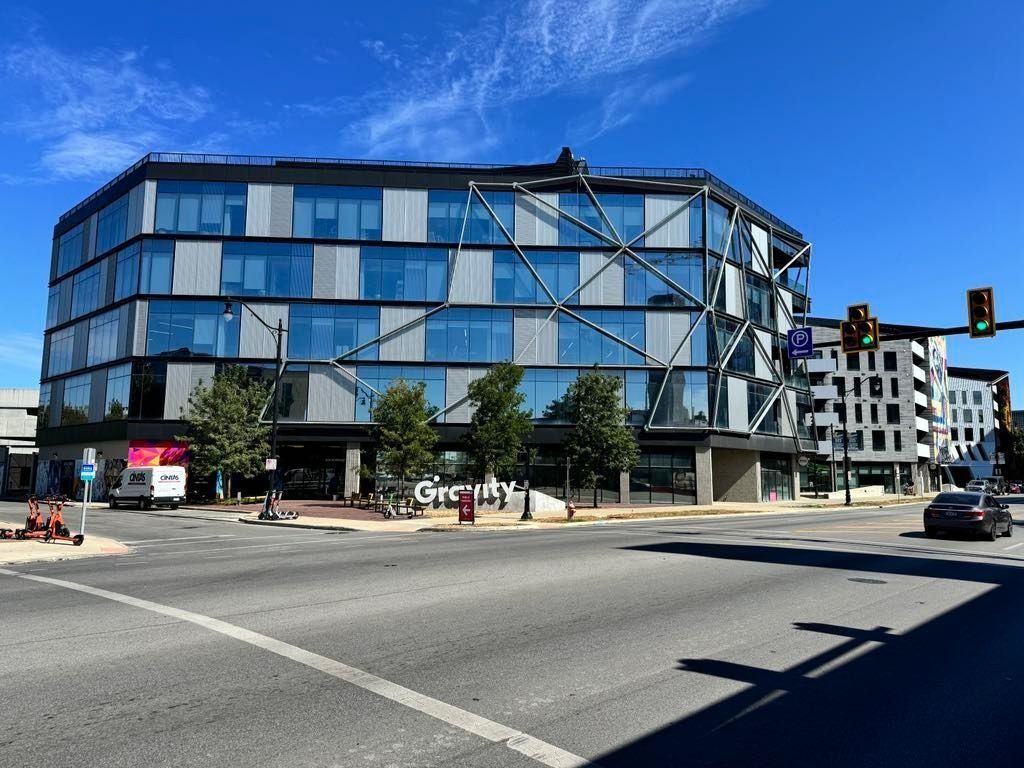Modern glass office building at a city intersection under a clear blue sky