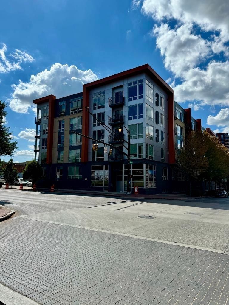 Modern apartment building on a street corner under a bright blue sky with clouds