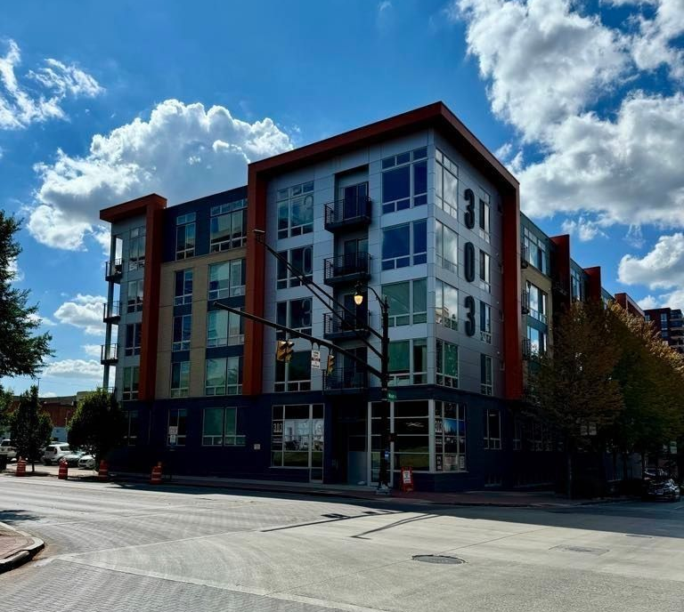 Modern apartment building on a street corner under a bright blue sky with clouds