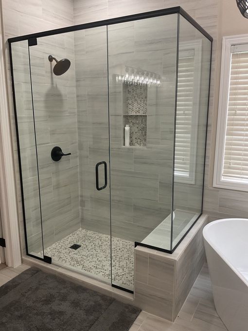 Glass walk-in shower with black trim, pebble floor, and built-in bench in a modern bathroom