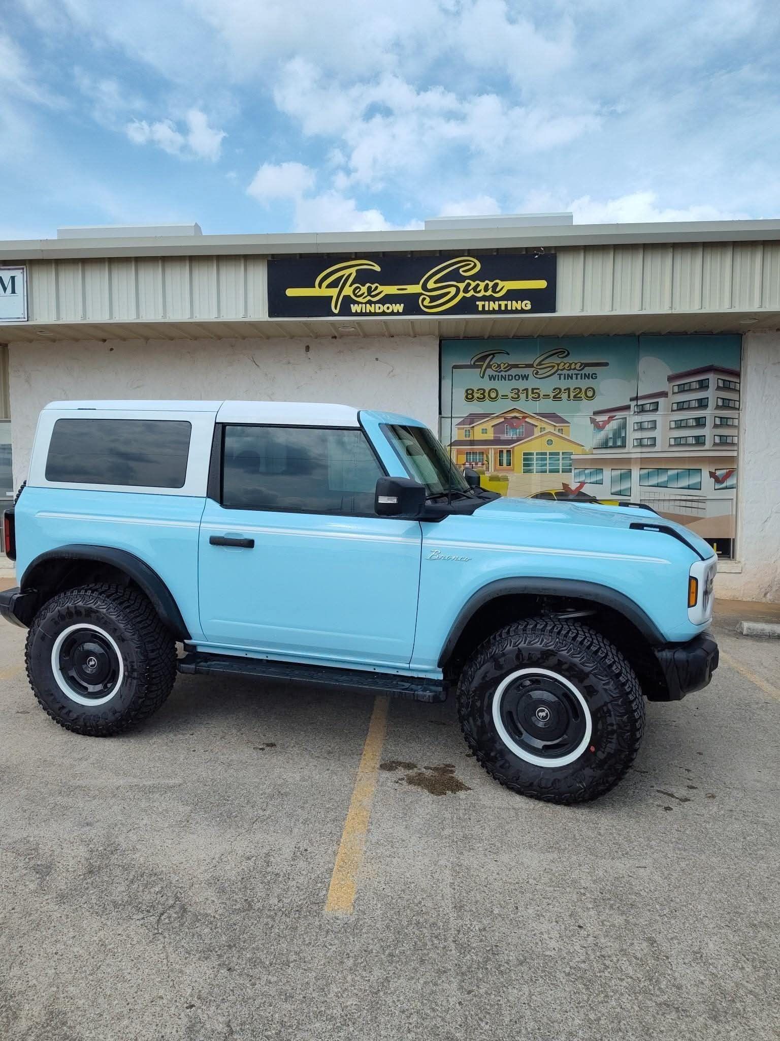 A blue ford bronco is parked in front of a building.