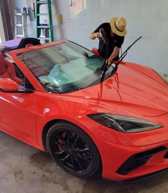 A man in a hat is cleaning the windshield of a red sports car