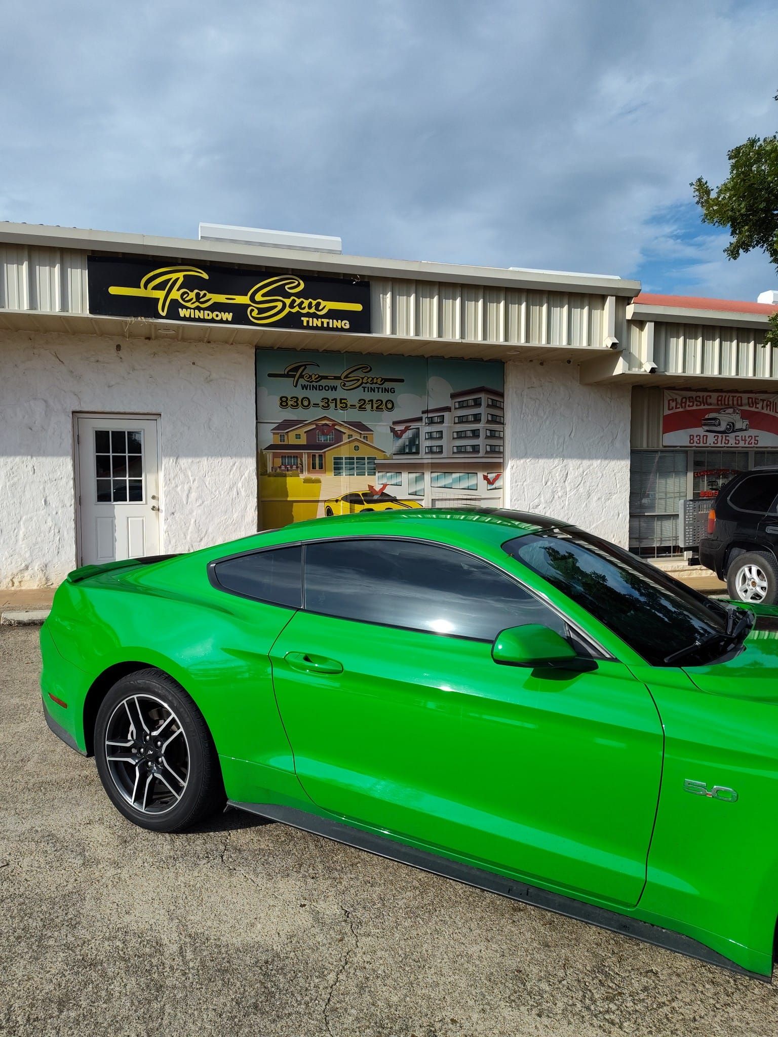 A green mustang is parked in front of a building.