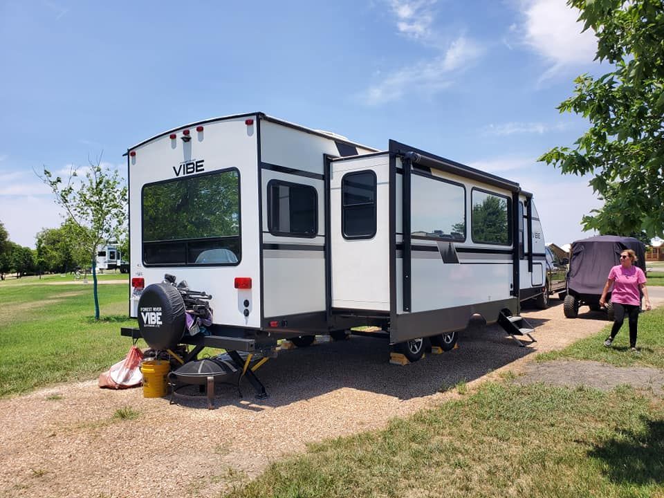 A woman is walking past a white rv parked in a grassy area.