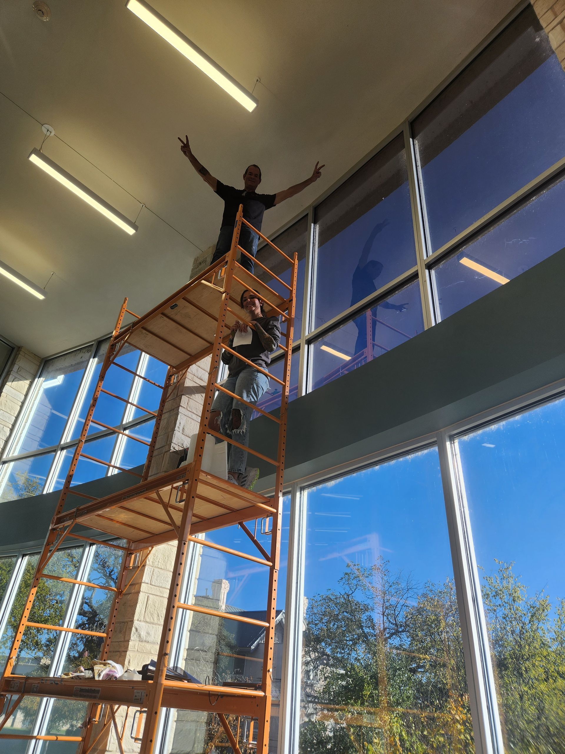 A man is standing on a scaffolding in front of a large window.