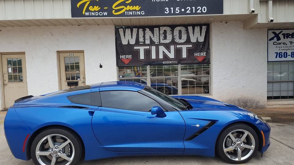 A blue corvette is parked in front of a window tint shop.