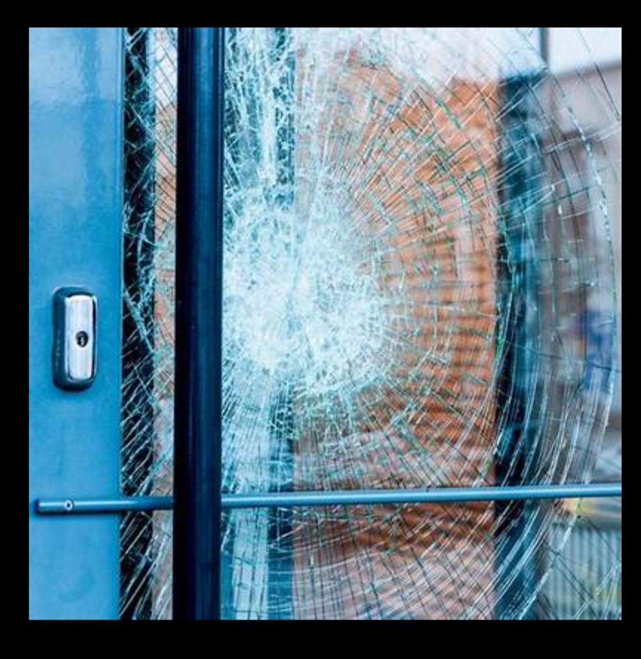 A close up of a broken glass door with a brick building in the background.