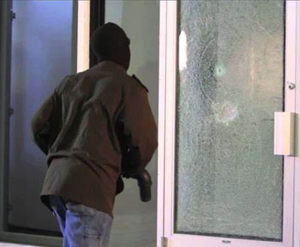 A man in a mask is standing in front of a glass door.