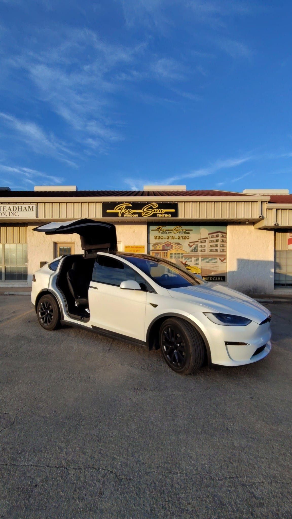 A white tesla model x is parked in front of a building with its trunk open.