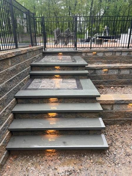 Stone steps with built-in lights, leading up to a patio area with a black fence.