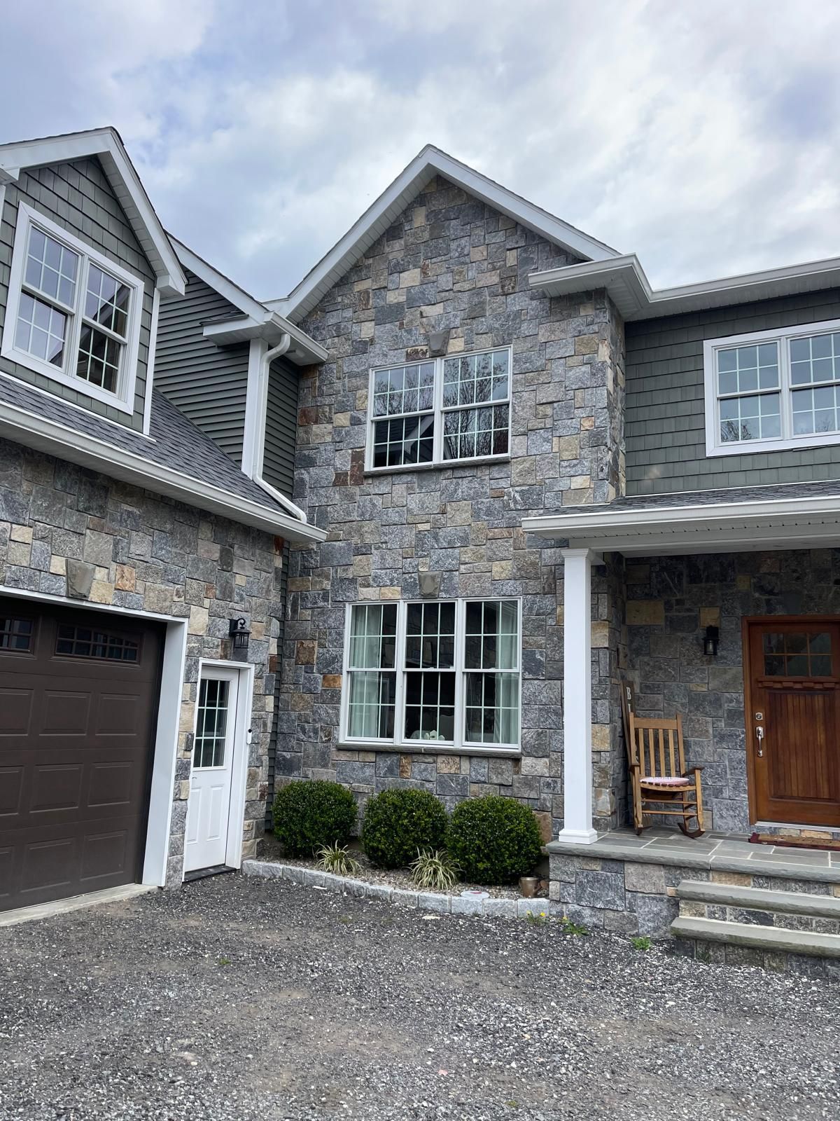 Stone-clad house with garage, windows, and front porch with pillars under a cloudy sky.