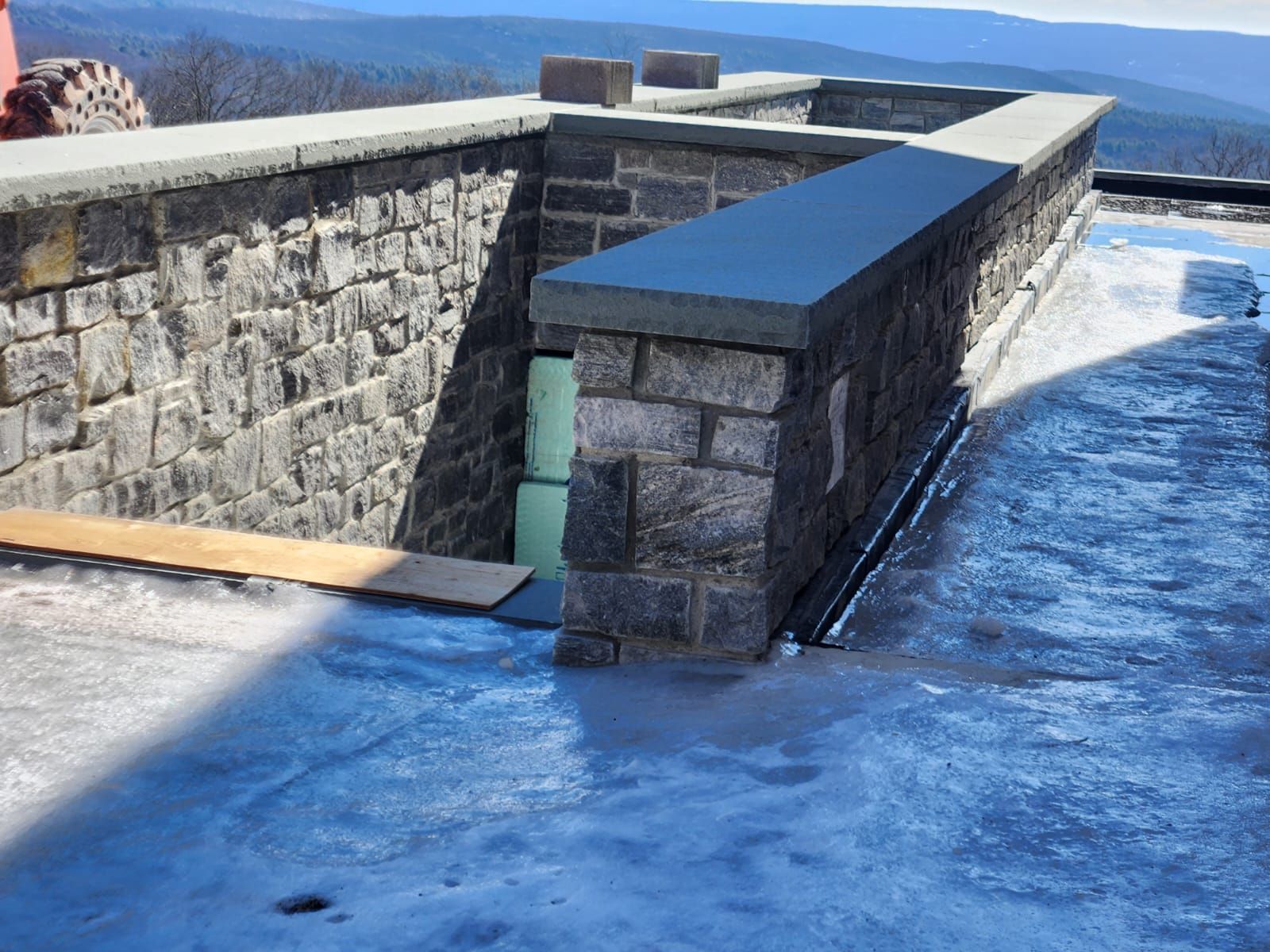 Stone wall with a concrete walkway on a rooftop, overlooking a mountain range.
