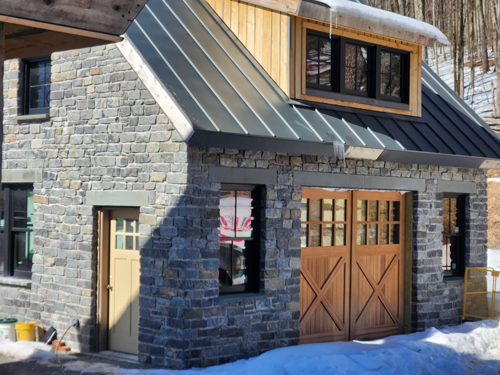 Stone building with wood doors and accents, metal roof, and small dormer with windows.