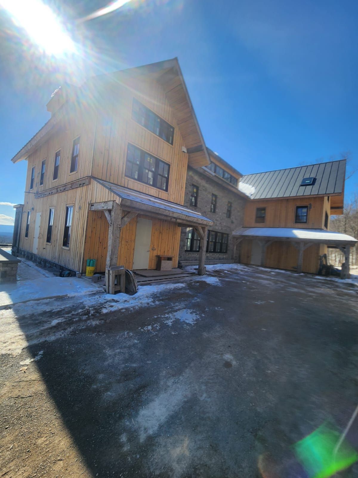 Unfinished wood-framed building with snow, clear sky, and a driveway.