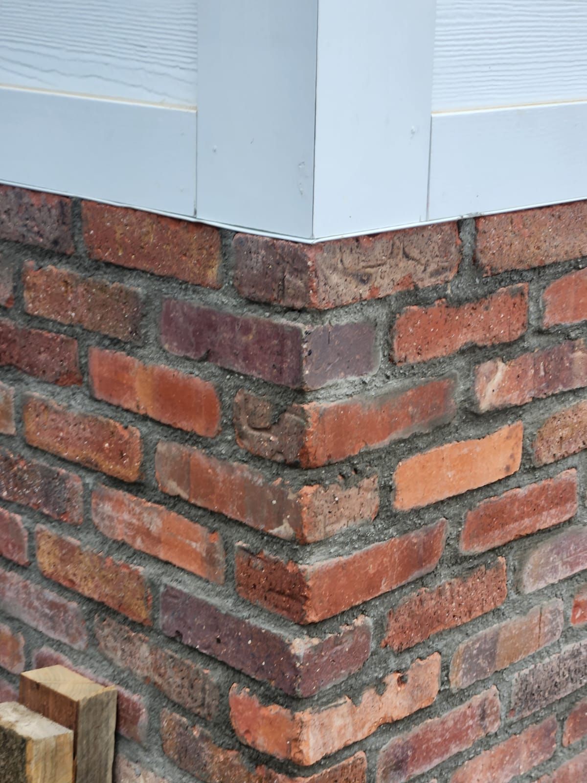 Corner of a brick wall with red and brown bricks and gray mortar, beneath a white structure.